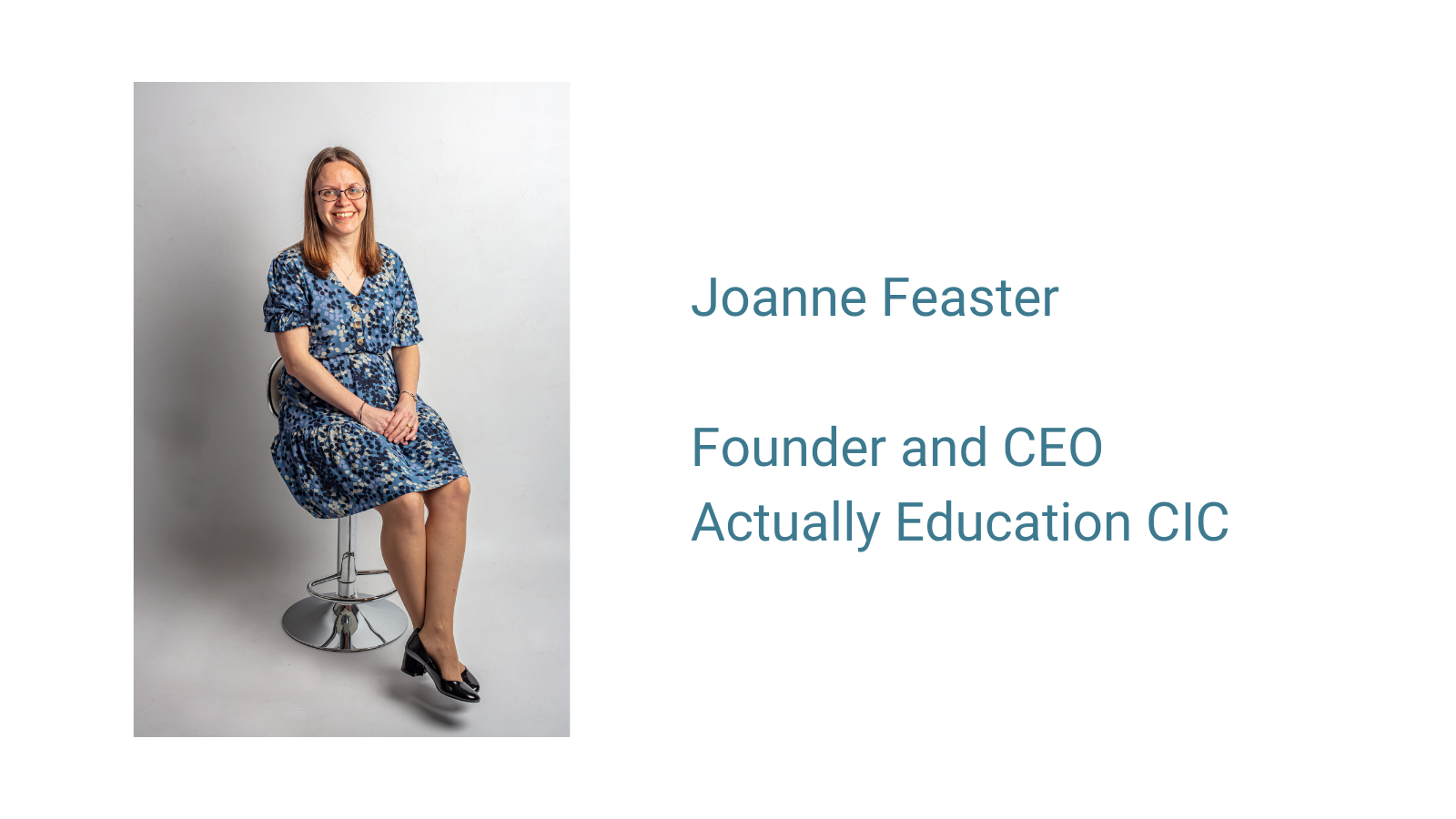 Picture of Joanne Feaster sitting on a chair with a blue dress and grey background. Founder and CEO of Actually Education CIC